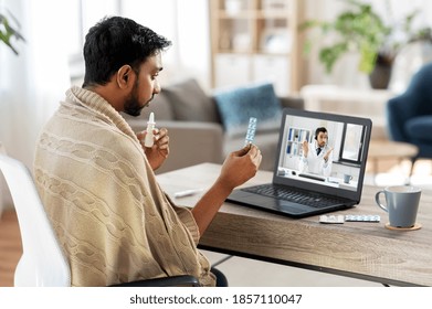 Healthcare, Technology And People Concept - Sick Indian Man In Blanket With Thermometer Having Video Call Or Online Consultation With Doctor On Laptop Computer At Home