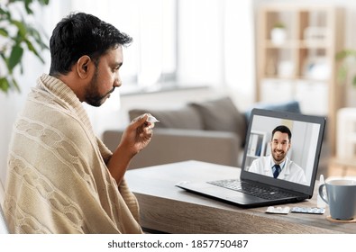 Healthcare, Technology And People Concept - Sick Indian Man In Blanket With Thermometer Having Video Call Or Online Consultation With Smiling Doctor On Laptop Computer At Home