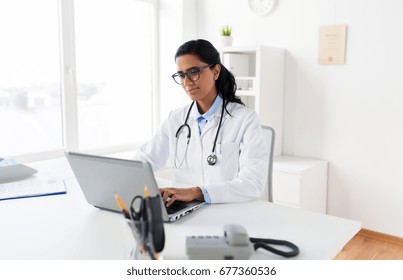 Healthcare, Technology People And Medicine Concept - Female Doctor In White Coat And Glasses Typing On Laptop Computer At Hospital