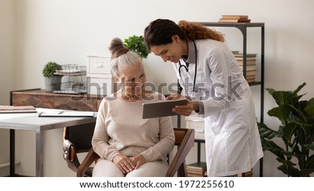 Healthcare and technology. Young latin female doctor consult sick aged lady in office at hospital using digital tablet. Millennial woman gp show older person patient lab test results on pad pc screen
