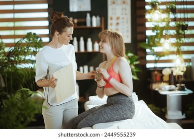 Healthcare time. smiling massage therapist woman in massage cabinet with clipboard, teenage client and golden medal. - Powered by Shutterstock