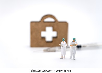 Healthcare And Vaccine Consept. Two Doctor Miniature Figure People With Patient File Standing With Syringe And Wooden Bag With Cross Logo On White Background.