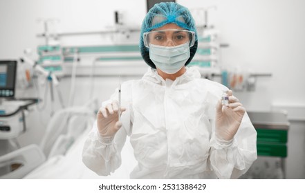 A healthcare worker in full protective gear holds up a syringe and a vaccine vial in a hospital room, ready for an injection, highlighting vaccination, medical safety, and healthcare protocols. - Powered by Shutterstock