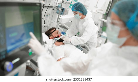 Healthcare worker in full protective gear adjusts breathing mask on male patient in hospital bed, surrounded by medical equipment, highlighting critical care, respiratory support, patient treatment - Powered by Shutterstock