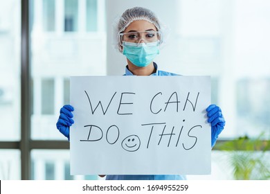Healthcare worker holding placard with supportive 'we can do this' message while standing in the hospital. 
