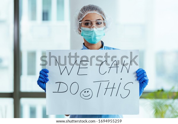 Healthcare worker\
holding placard with supportive \'we can do this\' message while\
standing in the hospital.\

