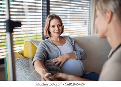 Healthcare Worker With IV Drip Examining Pregnant Woman Indoors At Home.