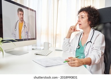 Healthcare Worker Talking To Coworker On Video Call Over Computer While Sitting At Office