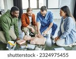 healthcare worker tamponing wound on simulator with bandage while showing life-saving skills to multicultural team near CPR manikin, defibrillator and medical equipment, emergency response concept