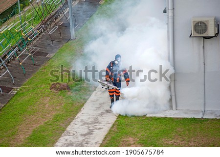Healthcare worker using Fogging machine spraying chemical to eliminate mosquitoes and kill larvae to fight against the spread of dengue fever, Zika virus or Malaria at a residential area.