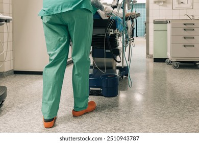 A healthcare worker wearing surgical attire moves an operating room table - Powered by Shutterstock