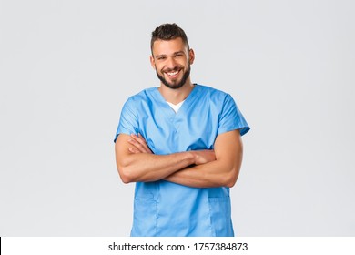 Healthcare Workers, Medicine, Covid-19 And Pandemic Self-quarantine Concept. Smiling Handsome, Hispanic Doctor, Male Nurse In Blue Scrubs, Cross Arms Chest, Laughing Camera Cheerful