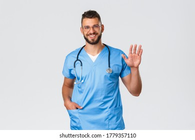 Healthcare Workers, Medicine, Covid-19 And Pandemic Self-quarantine Concept. Friendly Doctor, Male Nurse In Scrubs And Stethoscope, Saying Hi To Patient Or Coworker, Wave Hand In Hello