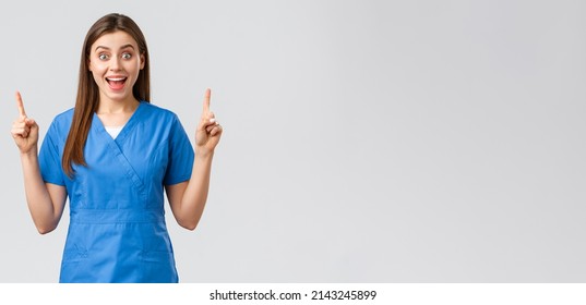 Healthcare workers, prevent virus, insurance and medicine concept. Excited, happy nurse or doctor in blue scrubs smiling from good news, pointing fingers up, show patients great news - Powered by Shutterstock