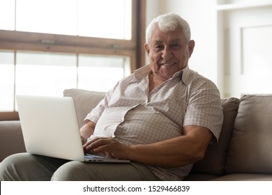 Healthy 80s old man seated on couch with laptop smiles looking at camera, enjoy time in internet, easy usage of medical apps for elderly patient online chat with doctor convenient program use concept