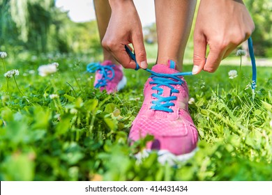 Healthy active lifestyle woman athlete tying running shoes. Happy sporty runner girl lacing shoelaces on pink fashion sneakers on summer grass in city park getting ready for a fitness morning jog.
