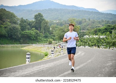 Healthy And Active Millennial Asian Man In Sportswear Running Or Jogging At The Beautiful Lake, Training Before Long Marathon. Healthy Lifestyle Concept