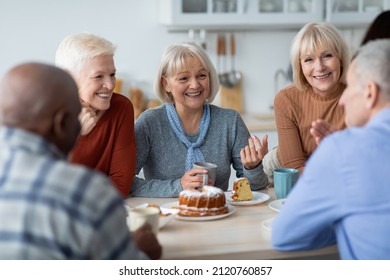 Healthy and active positive senior people of different nationalities sitting at kitchen, drinking tea and eating cake together, having conversation and laughing, chilling together at nursing home - Powered by Shutterstock