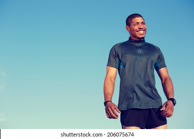 Healthy African American Runner Standing At Sunset On Blue Sky Background, Portrait Of Attractive Athlete Smiling And Looking Away, Fitness And Healthy Lifestyle Concept