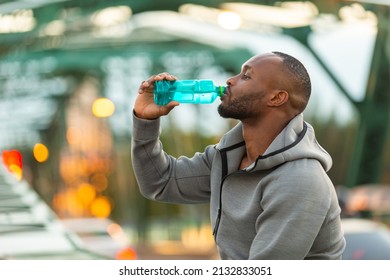 Healthy African man in sportswear drinking water from a bottle while jogging on the bridge in the city at summer sunset. Strong male athlete enjoy outdoor lifestyle sport training running workout.  - Powered by Shutterstock