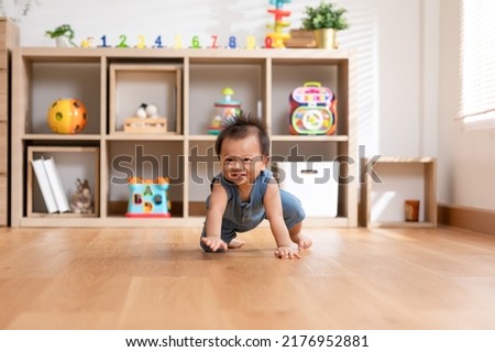 Healthy asian baby toddler crawling on floor to learn to crawl indoors. Adorable baby keeping her belly and legs down on the floor to belly crawl fun and happiness at home