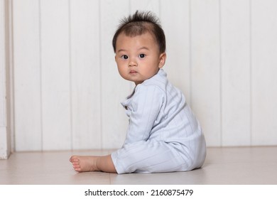 Healthy Asian Baby Toddler Sitting On Floor To Learn To Crawl Indoors Looking At Camera. Adorable Baby Looking Around On The Floor Indoors At Home