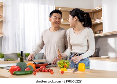 Healthy Asian Family Preparing Delicious Meal Full Of Vitamins And Minerals, Cheerful Husband And Wife Making Vegetable Salad, Cooking Dinner Together At Home, Having Conversation, Copy Space