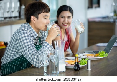 Healthy Asian Man Happy To Drink Smooth, Tasty Milk With Girlfriend Smiling As Enjoy Having Breakfast Of Natural Vegan Diet From Vegetable And Sauce. Couples Together Eat Homemade Food At Kitchen.