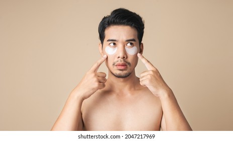 Healthy Asian Man Shirtless Pointing Show Patches Mask Under Eyes For Anti Wrinkles And Eye Dark Circles On Face. Isolated On Brown Color Background.