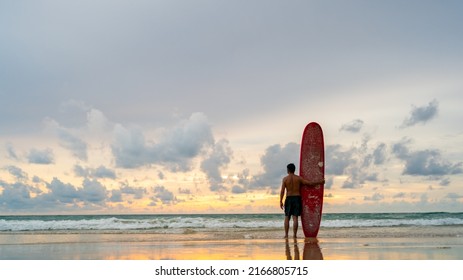 Healthy Asian Senior Man Surfer In Swimwear Holding A Surfboard On The Beach At Summer Sunset. Wellness Elderly Retired Male Enjoy Outdoor Activity Lifestyle And Water Sport Surfing On Summer Vacation