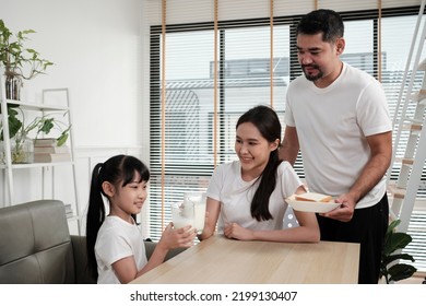 A Healthy Asian Thai Family, Daughter, And Young Mum Drink Fresh White Milk In Glass And Bread From Father, Joy Together At A Dining Table In Morning, Wellness Nutrition Home Breakfast Meal Lifestyle.