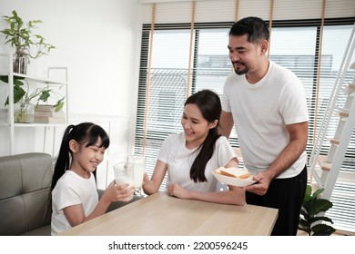 A Healthy Asian Thai Family, Daughter, And Young Mum Drink Fresh White Milk In Glass And Bread From Father, Joy Together At A Dining Table In Morning, Wellness Nutrition Home Breakfast Meal Lifestyle.