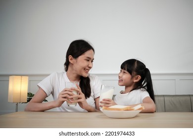 A Healthy Asian Thai Family, Little Daughter, And Young Mother Drink Fresh White Milk In Glass And Bread Joy Together At A Dining Table In Morning, Wellness Nutrition Home Breakfast Meal Lifestyle.