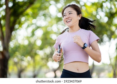 Healthy Asian woman smiling while running in the park in the morning. She is exercising while listening to music.