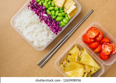 Healthy Asian-style Vegan Bento Box With Rice, Fried Tofu, Edamame Beans And Cherry Tomatoes And Pieces Of Pineapple With Metal Chopsticks On Side, Flatlay