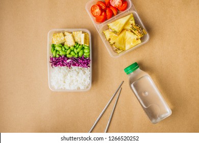 Healthy Asian-style Vegan Bento Box With Rice, Fried Tofu, Edamame Beans And Cherry Tomatoes And Pieces Of Pineapple With Metal Chopsticks On Side, Flatlay