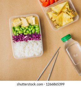 Healthy Asian-style Vegan Bento Box With Rice, Fried Tofu, Edamame Beans And Cherry Tomatoes And Pieces Of Pineapple With Metal Chopsticks On Side, Flatlay