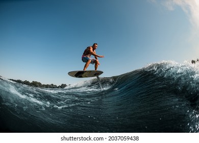 healthy athletic man balancing on the wave with hydrofoil foilboard on background of blue sky. Surfing, entertainment, leisure, water sports