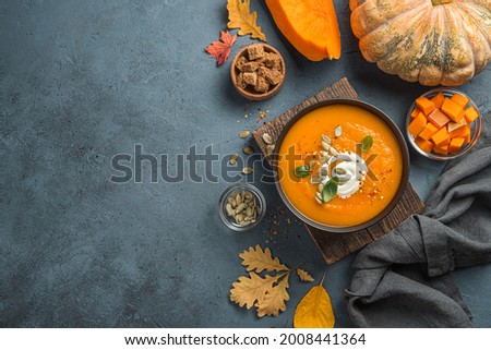 Healthy, autumn pumpkin cream soup with cream and basil on a dark blue background with autumn foliage. Top view, copy space.