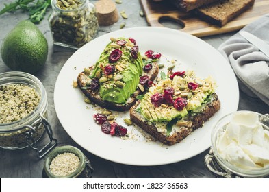 Healthy avocado toasts for breakfast or lunch with rye bread, cream cheese, arugula, sliced avocado, dried cranberry, pumpkin, hemp and sesame seeds. Vegetarian sandwiches. Clean eating. Top view.