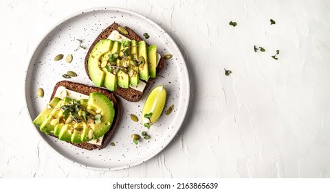 Healthy avocado toasts with rye bread, sliced avocado, cheese, pumpkin, nut and sesame for breakfast or lunch. Vegetarian food. Vegan menu. Long banner format. top view.
