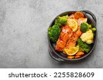 Healthy baked fish salmon steaks, broccoli, cauliflower, carrot in black cast iron casserole bowl on grey stone background. Cooking a delicious low carb dinner, healthy nutrition, space for text