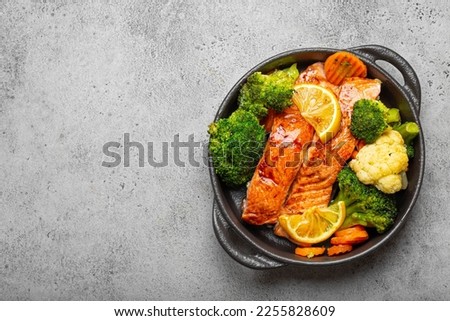 Healthy baked fish salmon steaks, broccoli, cauliflower, carrot in black cast iron casserole bowl on grey stone background. Cooking a delicious low carb dinner, healthy nutrition, space for text