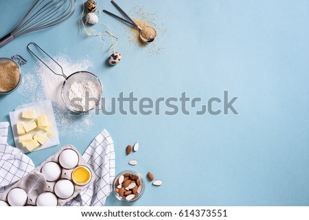 Healthy baking ingredients - flour, almond nuts, butter, eggs, biscuits over a blue table background. Bakery background frame. Top view, copy space.