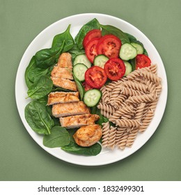 Healthy Balanced Food In White Plate On Green Background. Whole Grain Pasta, Spinach, Vegetables, And Chicken Breast