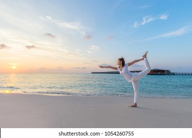 Healthy Beautiful Attractive Asian woman wearing white shirt practicing yoga King Dancer Pose on the beach in Maldives with sunset,comfortable and relax with yoga in holiday - Powered by Shutterstock