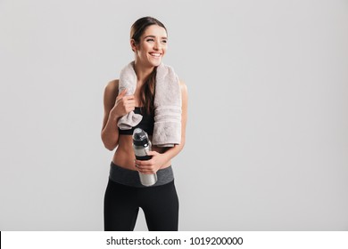 Healthy beautiful sportswoman wearing tracksuit with towel looking aside and holding bottle with fresh water isolated over gray background - Powered by Shutterstock