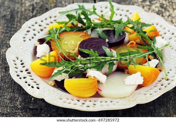 Healthy Beet Salad with red,\
white, golden beets, arugula, nuts, feta cheese on wooden\
background
