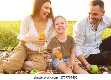 Healthy Beverages. Portrait Of Laughing Family Sitting On Blanket And Drinking Orange Juice From Glasses