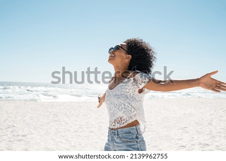 Healthy black woman standing on the beach with copy space. Happy young african american woman with open arms at seaside. Freedom girl dancing and daydreaming at beach during summer vacation.